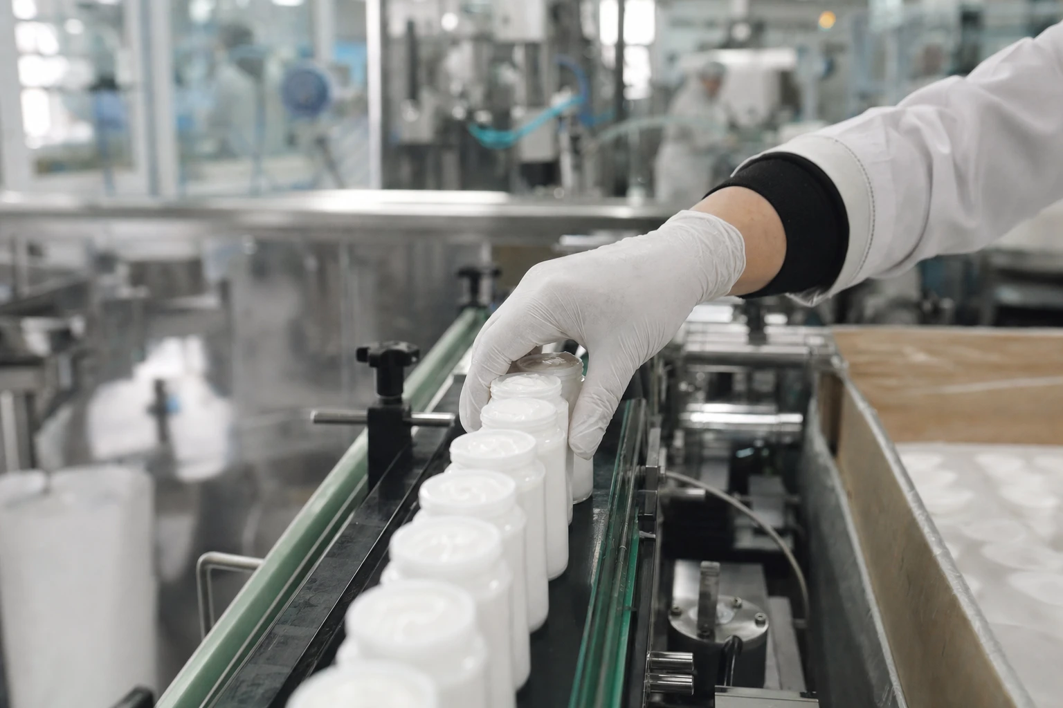 Gloved technician handling cosmetic product containers on the production line at Ausmetix